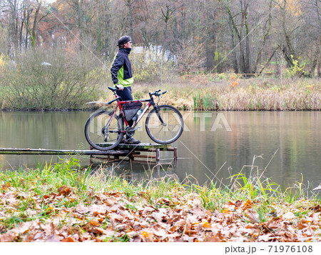 Cyclist stay at his trekking bike on small pond pier and watching swans 71976108