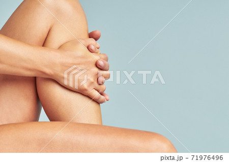 Cropped shot of a woman touching her soft and silky skin on legs after epilation while sitting over blue background 71976496