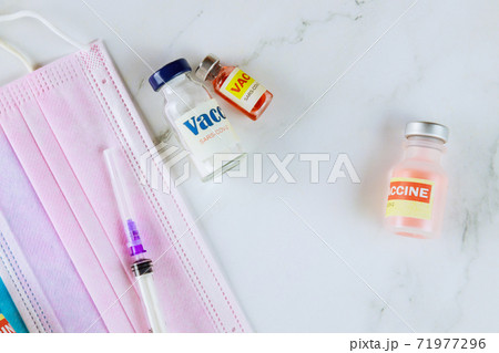 Coronavirus vaccine SARS-CoV-2 bottles and syringe for injection to fight the pandemic on protective surgical mask Coronavirus vaccine SARS-CoV-2 bottles and syringe for injection to fight the pandemic on protective surgical mask 71977296