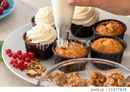 Closeup view of female baker hand decorating tasty cupcake with whipped cream top 71977870