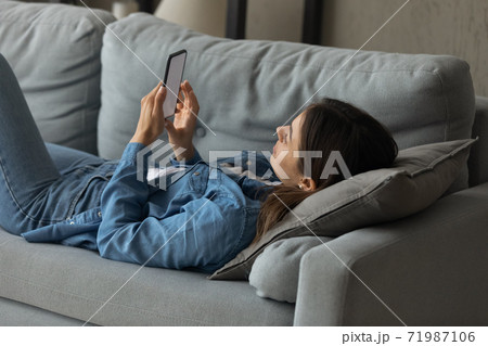 Young woman relax on couch using smartphone Young woman relax on couch using smartphone 71987106