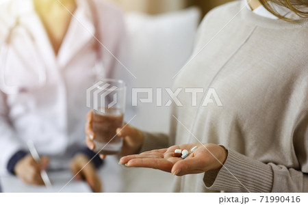 Close-up woman-patient holding pills near her doctor, time to take medications for headache. Stay at home concept during Coronavirus pandemic and self isolation quarantine. Covid 2019 Close-up woman-patient holding pills near her doctor, time to take medications for headache. Stay at home concept during Coronavirus pandemic and self isolation quarantine. Covid 2019 71990416