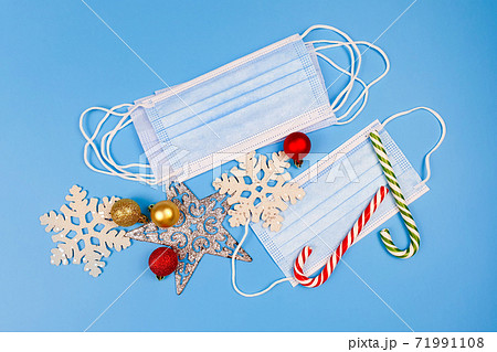 Blue protective medical masks,  christmas or new year decor and striped candy cane on a blue background. Top view. 71991108