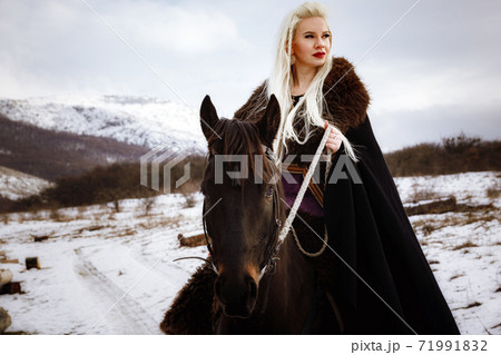 Woman viking with a black horse against the background of mountains Woman viking with a black horse against the background of mountains 71991832
