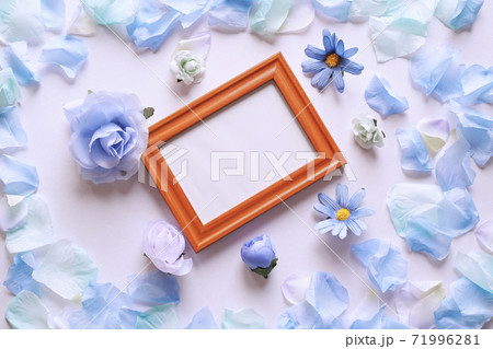 白背景に青色の造花と花びら。中央に斜めの木製フォトフレームと白いコピースペース。平置きの俯瞰撮影。 71996281