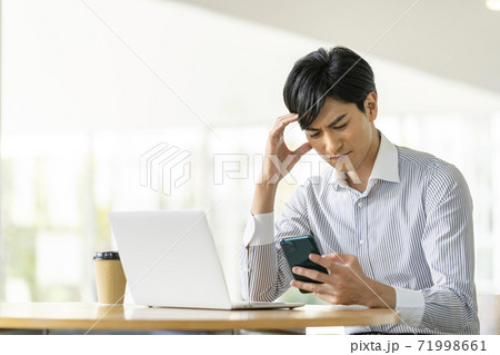 スマートフォンの画面を見ながら頭を抱える若い男性 71998661