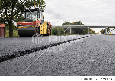 Asphalt road roller with heavy vibration roller compactor press new hot asphalt on the roadway on a road construction site. Heavy Vibration roller at asphalt pavement working. Repairing. 71999473