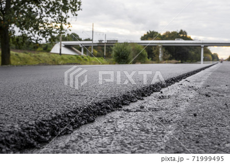 A large layer of fresh hot asphalt. Layer of asphalt raw material in a shallow depth of field. Rollers rollin fresh hot asphalt on the new road. Road construction. Construction of a new road. 71999495