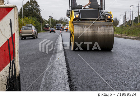 Asphalt road roller with heavy vibration roller compactor press new hot asphalt on the roadway on a road construction site. Heavy Vibration roller at asphalt pavement working. Repairing. Asphalt road roller with heavy vibration roller compactor press new hot asphalt on the roadway on a road construction site. Heavy Vibration roller at asphalt pavement working. Repairing. 71999524