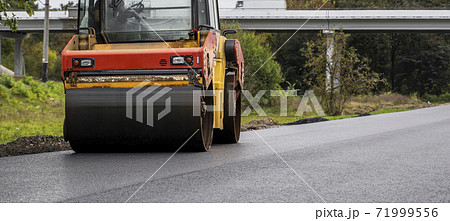 Asphalt road roller with heavy vibration roller compactor press new hot asphalt on the roadway on a road construction site. Heavy Vibration roller at asphalt pavement working. Repairing. 71999556