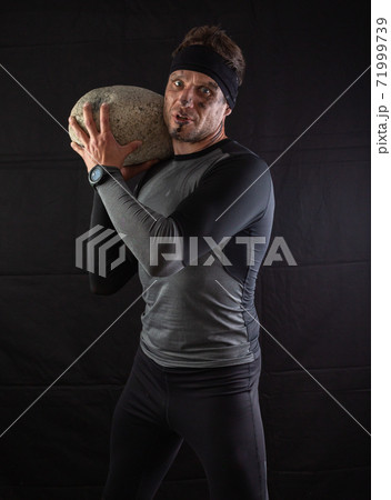 Sporty man holding a large heavy stone in his hands on a black background Sporty man holding a large heavy stone in his hands on a black background 71999739