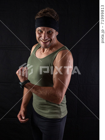 Handsome shirtless fitness man in gray shorts, smiling and posing against dark black background. Mild retouch, studio lighting. Handsome shirtless fitness man in gray shorts, smiling and posing against dark black background. Mild retouch, studio lighting. 71999813
