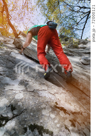An adult bearded man in the age is practicing rock climbing on a home spot a large rock in the forest in a sunny day 72000121