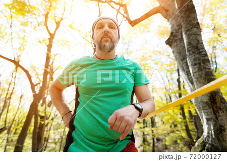 Portrait of a bearded man in age stands near a taut slackline in an autumn forest 72000127