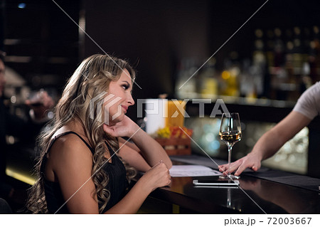 cute blonde girl ordered wine from the bartender in a nightclub 72003667