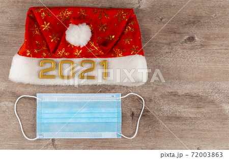 Santa Claus hat and surgical medical mask on a wooden background. coronavirus pandemic.  72003863