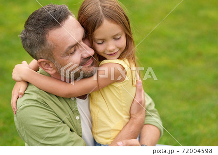 Portrait of happy young father and adorable little daughter hugging each other, standing with eyes closed while spending time in the green park on a summer day Portrait of happy young father and adorable little daughter hugging each other, standing with eyes closed while spending time in the green park on a summer day 72004598
