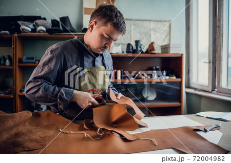 A talented young guy helps his father in the family business, cuts out blanks for shoes from leather 72004982