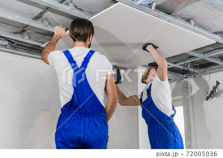 Adjusters are assembling a plasterboard ceiling using a drill Adjusters are assembling a plasterboard ceiling using a drill 72005036