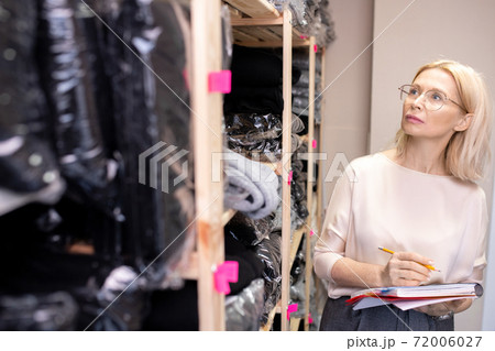 Blond mature shop assistant with pencil and copybook working in storage room Blond mature shop assistant with pencil and copybook working in storage room 72006027