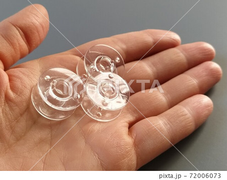 Transparent plastic bobbins from a modern sewing machine in the palm of a woman - a seamstress. Gray background. sewing machines Transparent plastic bobbins from a modern sewing machine in the palm of a woman - a seamstress. Gray background. sewing machines 72006073