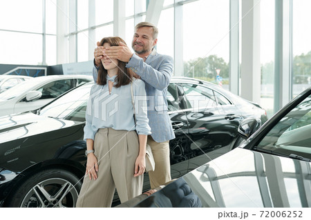 Happy mature man covering eyes of his wife standing between two new cars 72006252