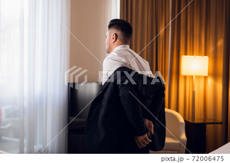 A young man taking off his jacket in a hotel room, rear view A young man taking off his jacket in a hotel room, rear view 72006475