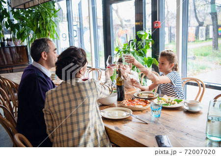 A family of four raising glasses at dinner in a cafe 72007020
