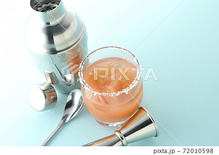 グラスの縁に塩が付いているピンクソルティドッグとカクテルシェーカーとメジャーカップ 72010598