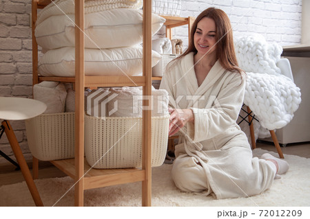 Young woman in warm robe is organizing linen closet with neatly folded towels, sheets and blankets. Young woman in warm robe is organizing linen closet with neatly folded towels, sheets and blankets. 72012209