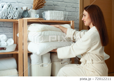Cheerful young beautiful woman pulls out pillows from the top shelf. . Copy space. Storage clothes. Cheerful young beautiful woman pulls out pillows from the top shelf. . Copy space. Storage clothes. 72012211