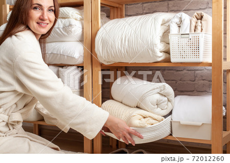 Young woman in warm robe is organizing linen closet with neatly folded towels, sheets and blankets. Young woman in warm robe is organizing linen closet with neatly folded towels, sheets and blankets. 72012260