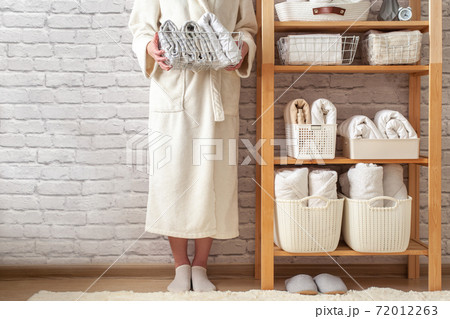 Woman in robe standing and holding white wire basket of folded bed sheets near bathroom linen closet Woman in robe standing and holding white wire basket of folded bed sheets near bathroom linen closet 72012263