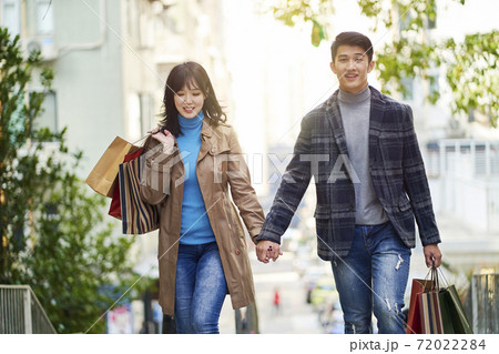 happy young asian couple walking on street in the city with shopping bags in hands happy young asian couple walking on street in the city with shopping bags in hands 72022284