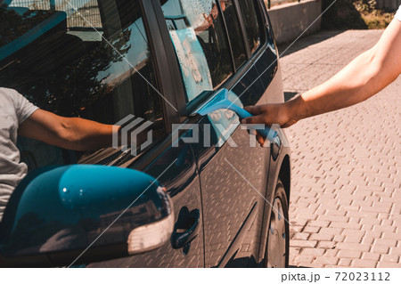 The man takes the remnants of water from the glass after washing the car at the self-service car wash, the car is blue. The man takes the remnants of water from the glass after washing the car at the self-service car wash, the car is blue. 72023112