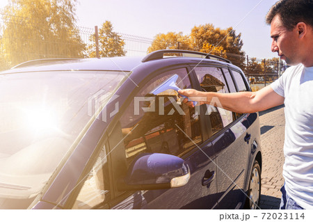 The man takes the remnants of water from the glass after washing the car at the self-service car wash, the car is blue. The man takes the remnants of water from the glass after washing the car at the self-service car wash, the car is blue. 72023114