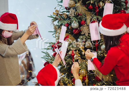 Girls decorate the Christmas tree with protective masks. Girls decorate the Christmas tree with protective masks. 72023488