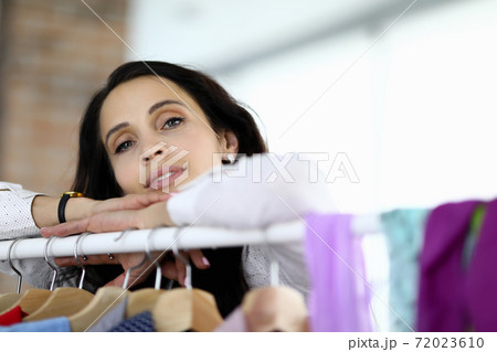 Female consultant stands next to hanger with clothes. Female consultant stands next to hanger with clothes. 72023610