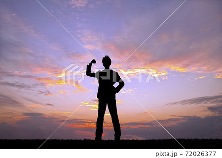 夕陽を背景にガッツポーズをするビジネスマンのシルエットの写真素材