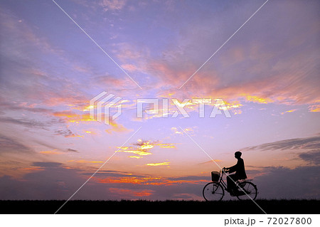 夕陽を背景に自転車通学する男子学生のシルエットの写真素材