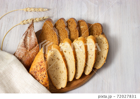 Slices of fresh homemade baguettes with whole grain on wooden board. White wooden background. Top view. 72027831
