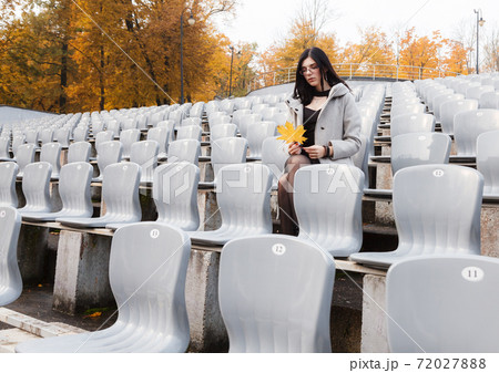 young girl in a gray coat sits on a seat of an empty stadium young girl in a gray coat sits on a seat of an empty stadium 72027888