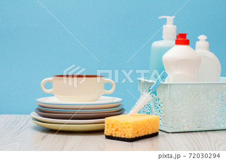 Bottles of dishwashing liquid in basket and plates on blue background. Bottles of dishwashing liquid in basket and plates on blue background. 72030294