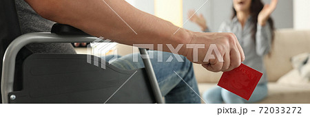 Man in wheelchair holds condom in hand close-up in front of joyful girl Man in wheelchair holds condom in hand close-up in front of joyful girl 72033272