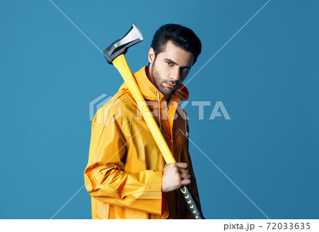 Young serious man in bright raincoat holding big ax on his shoulder 72033635