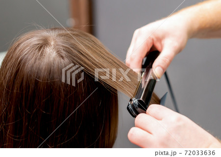 Hairdresser straightens hair of woman. 72033636