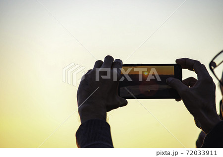 Hand holding the phone shooting the morning sun and the fog. Hand holding the phone shooting the morning sun and the fog. 72033911