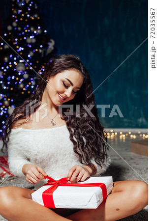 beautiful brunette woman at the Christmas tree with garland lights and gifts for the new year beautiful brunette woman at the Christmas tree with garland lights and gifts for the new year 72035567