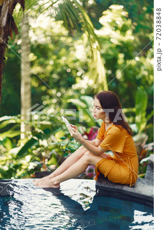 Woman in a yellow dress sitting by the pool in Bali Woman in a yellow dress sitting by the pool in Bali 72038848