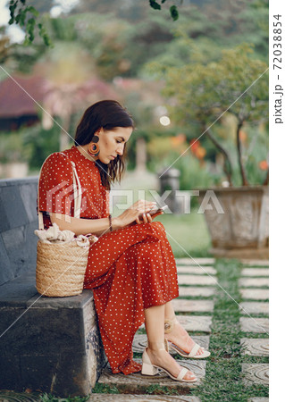 Girl in a red dress sitting and use the phone Girl in a red dress sitting and use the phone 72038854